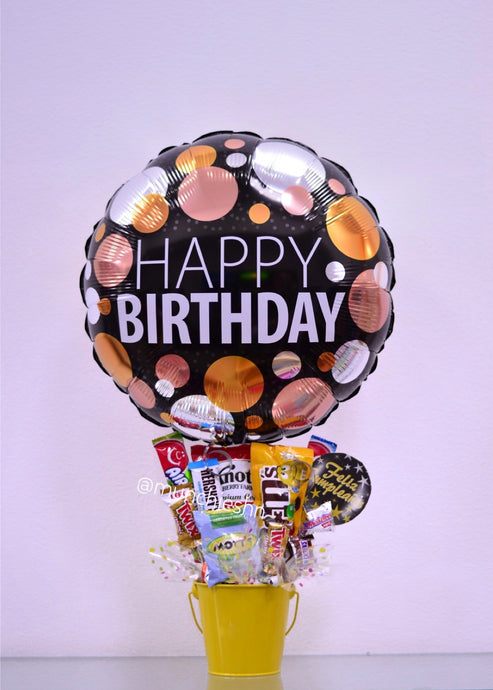 Arreglo de regalo con base de Cubeta metálica amarilla con dulces y chocolates americanos con globo grande negro de happy birthday,  ideal para expresar un feliz cumpleanos a una dama especial. Encuentralo en Tegucigalpa