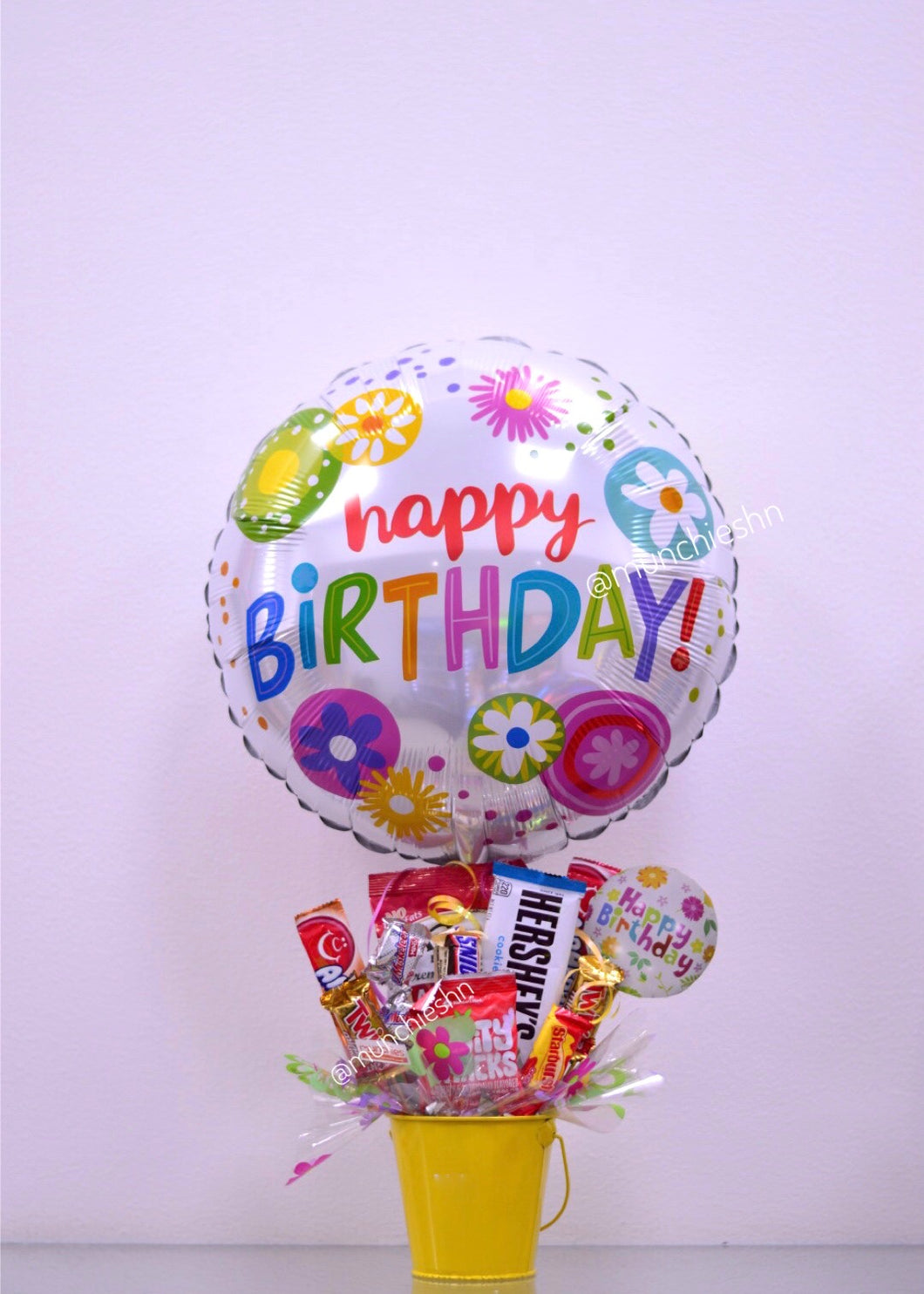 Arreglo de regalo con base de Cubeta metálica amarilla con dulces y chocolates americanos con globo grande gris flores happy birthday,  ideal para expresar un feliz cumpleanos a alguien especial. Encuentralo en Tegucigalpa