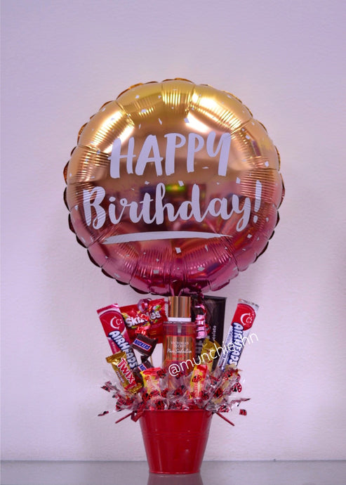 Arreglo de regalo con base de Cubeta metálica roja con dulces y chocolates americanos con globo grande dorado de happy birthday, incluye una fragancia original de Victoria's Secret ideal para expresar un feliz cumpleanos a una dama especial. Encuentralo en Tegucigalpa